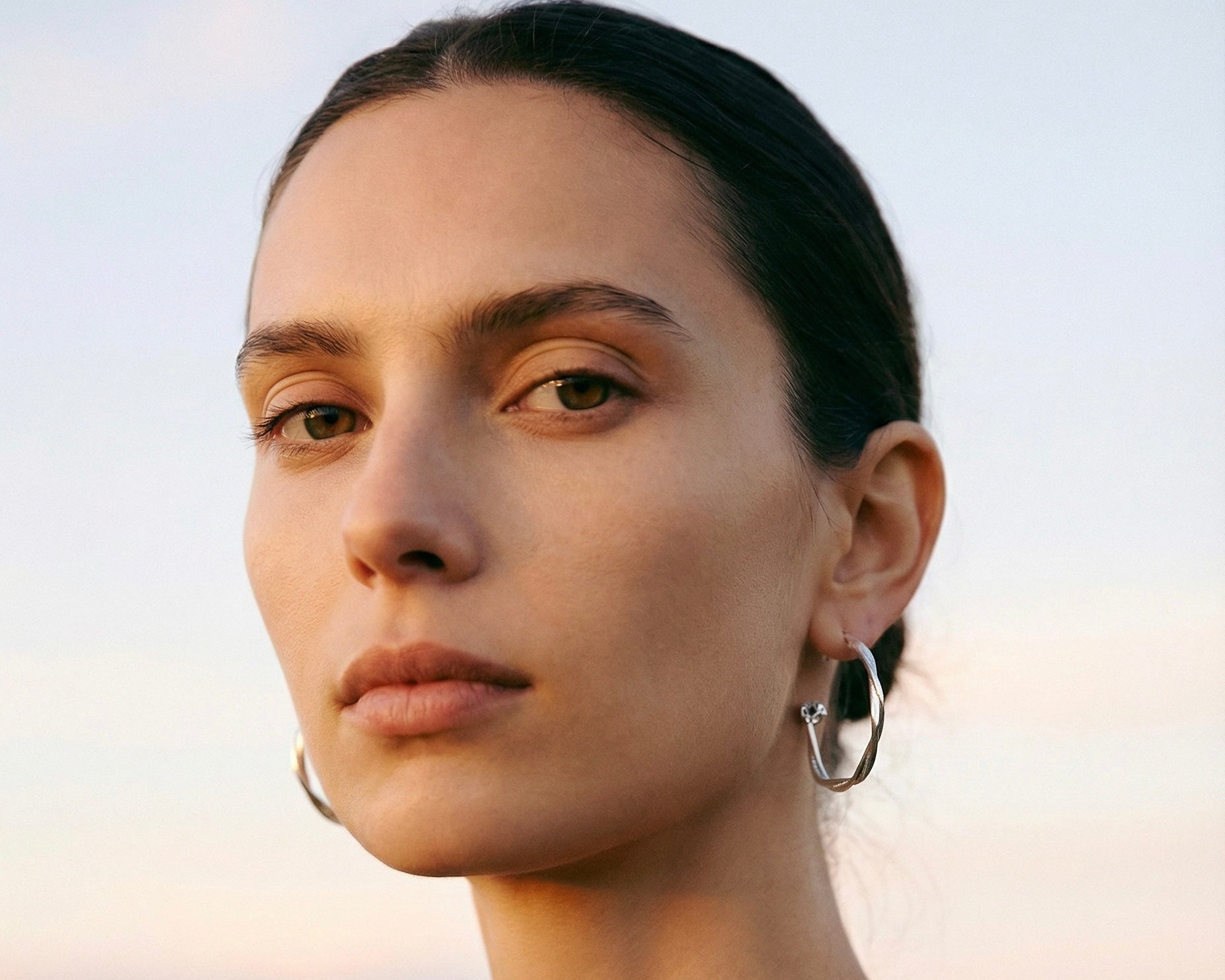 Model wearing Astraea Twist Hoop Earrings in sterling silver, showcasing sculptural twist design with Herkimer diamonds